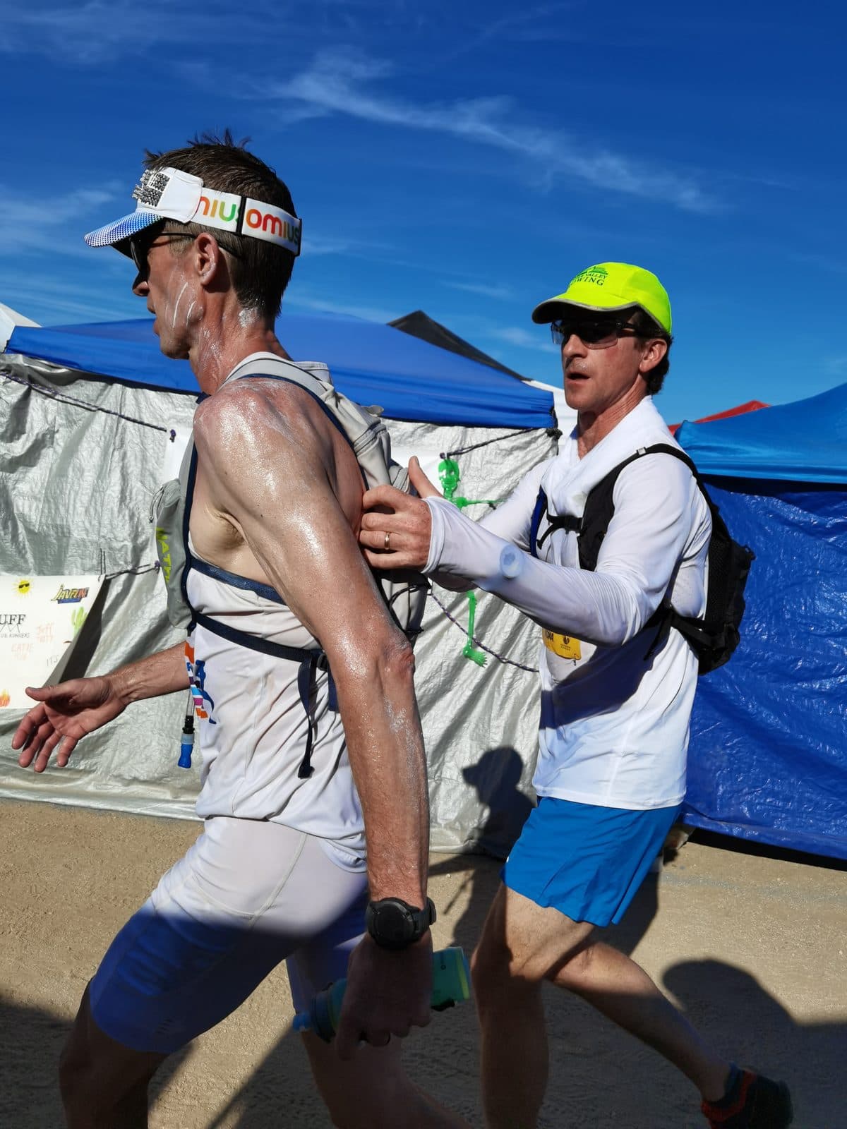 Matt Fitzgerald, sweat-soaked, runs through the aid station tents while his pacer Mike, in a yellow cap, adjusts his hydration pack